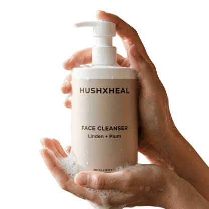 Two hands holding HUSHXHEAL Linden + Plum Face Cleanser 390 mL in a white pump bottle with a beige label, featuring water droplets and soft cleansing foam against a transparent background.